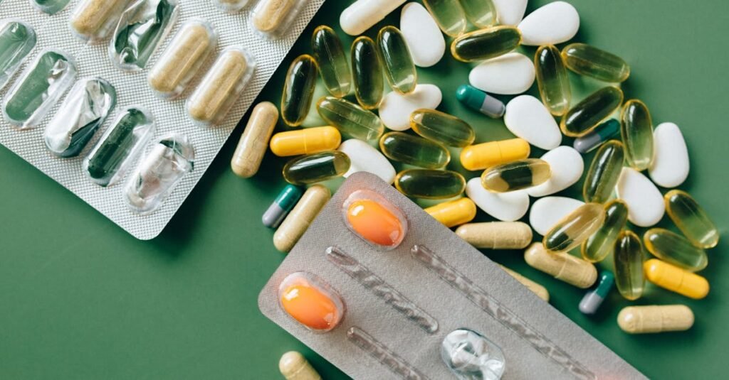 Variety of capsules and tablets laid out on a green surface for healthcare concept.